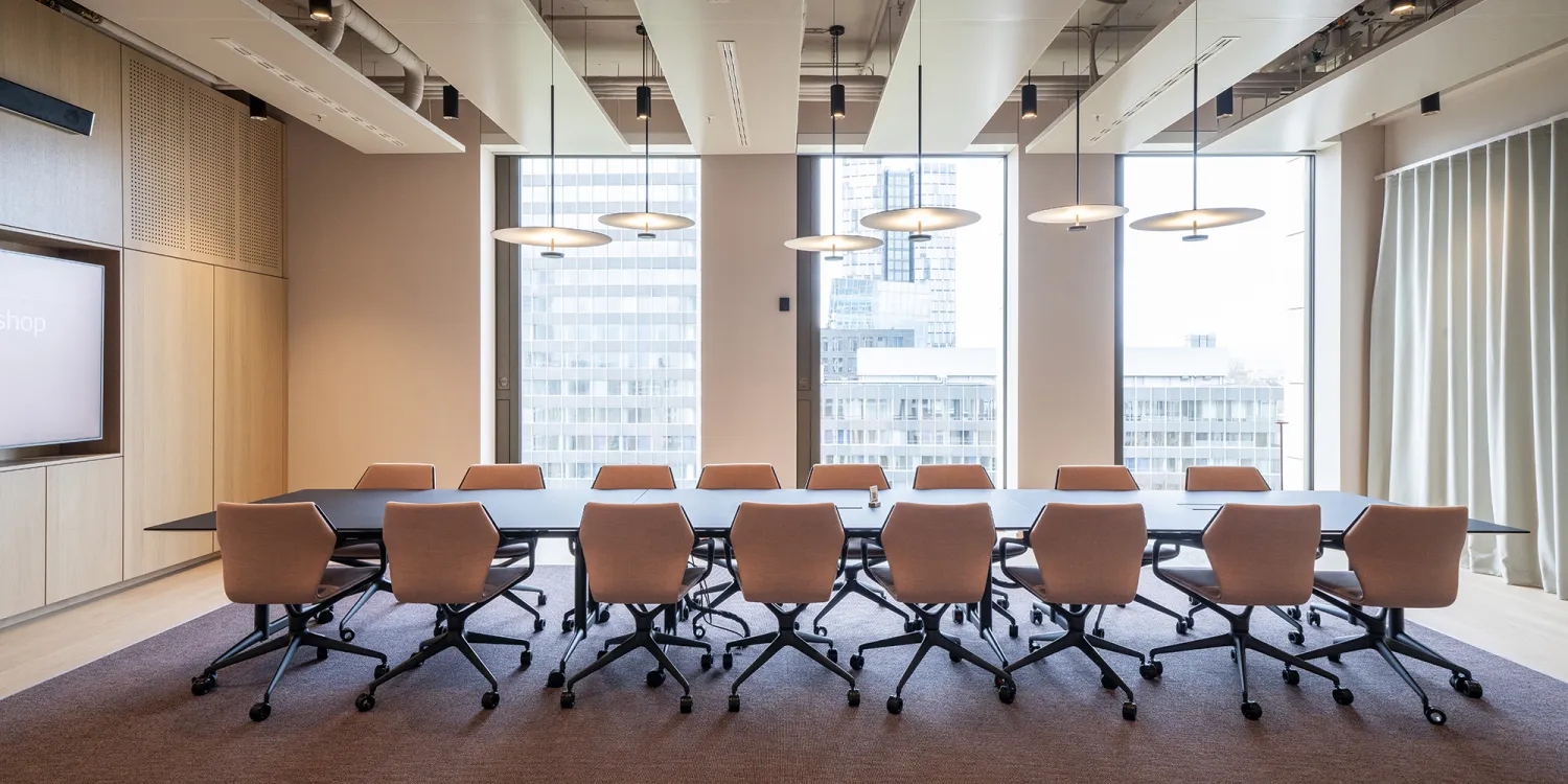 Großer Konferenzraum mit Blick auf die Skyline, dunklem Tisch, modernen Pendelleuchten und Akustikverkleidung.