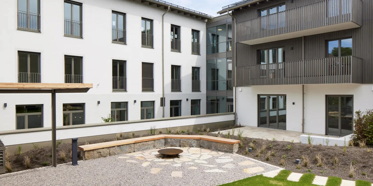 Begrünter Innenhof der VR Bank Andechs mit Sitzstufen, Natursteinmauern und harmonischer Architektur.