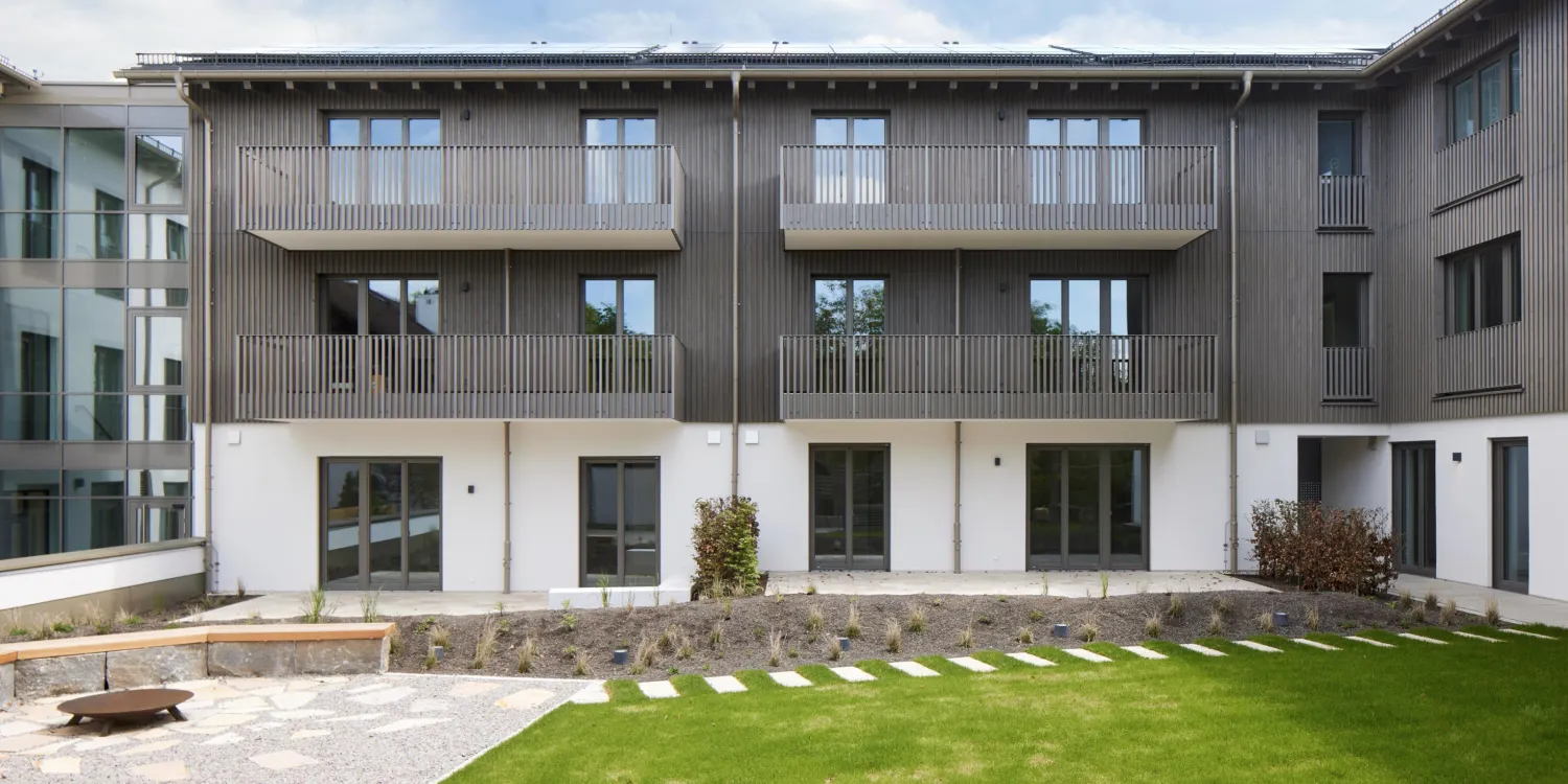 Gartenseite der VR Bank Andechs mit Holzfassade, Balkonen und einer begrünten Außenanlage.