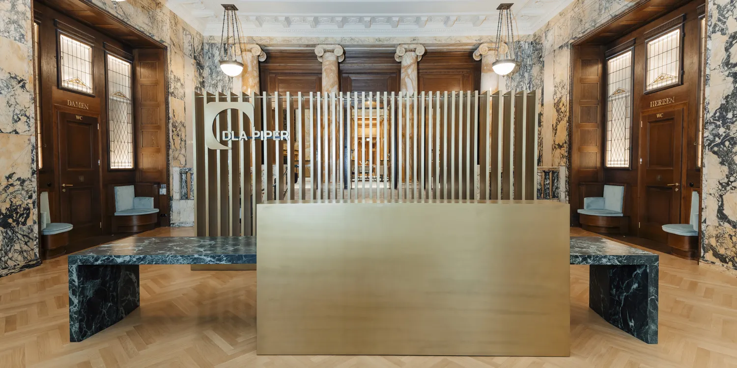 DLA Piper Wien: Empfangsbereich mit goldener Theke, blauen Sitzbänken und historischem Ambiente