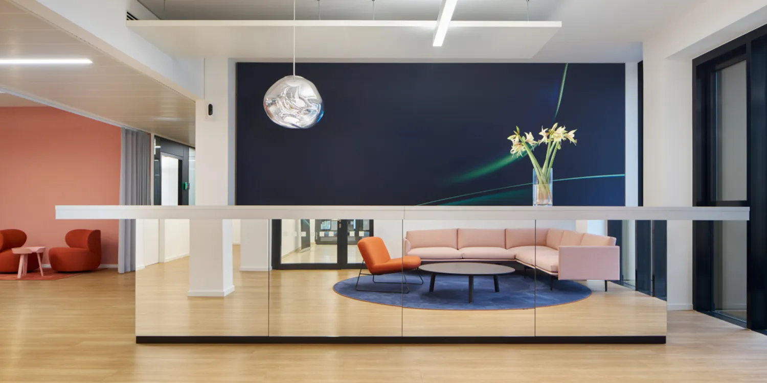 Elegante Lounge mit rosa Sofa, orangefarbenem Sessel, Spiegeltheke, Holzfußboden und skulpturaler Lampe.