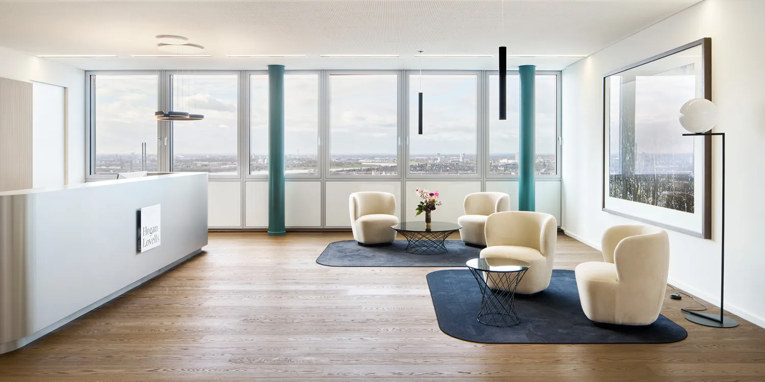 Eine elegante Lounge mit beigen Sesseln, schwarzen Tischen, Spiegelkugelleuchten und Blick auf den Fernsehturm.