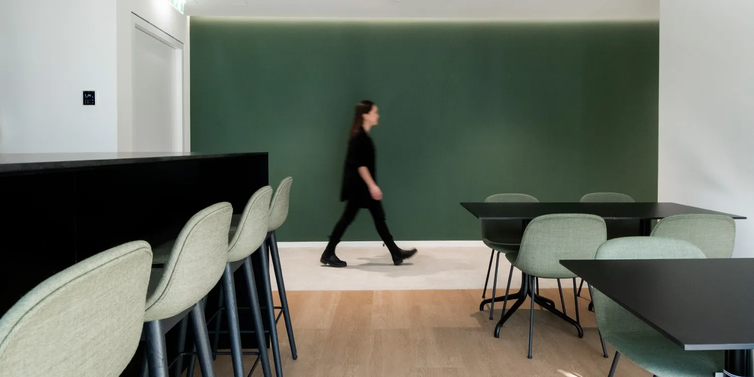 Guidehouse Sonycenter Berlin: Raum mit Sitzmöglichkeiten auf Barhocker oder Stuhl mit einer grünen Wand im Hintergrund