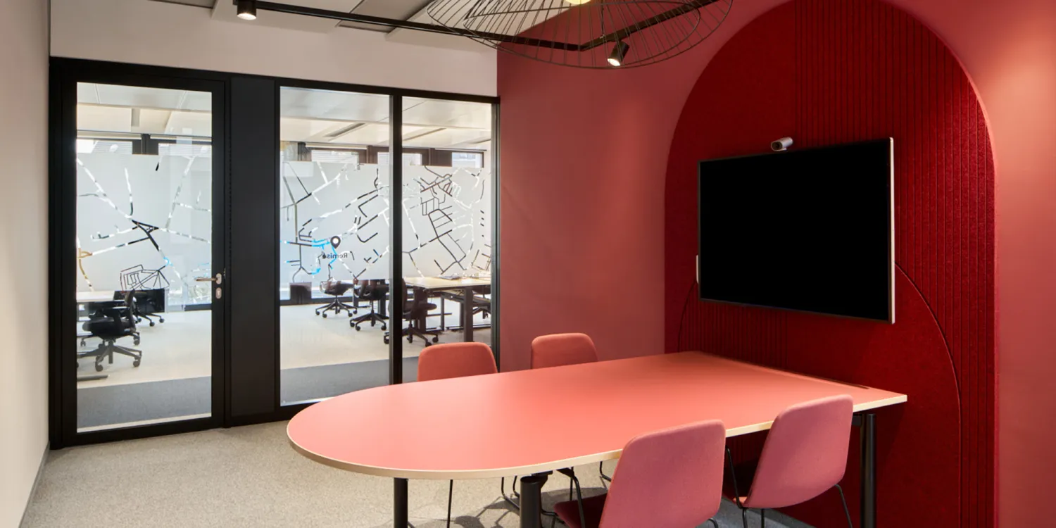 DLL Düsselorf – New Work: DLL Düsseldorf – Meetingraum in kräftigem Rot mit rundem Tisch, Wandnische und Bildschirm.