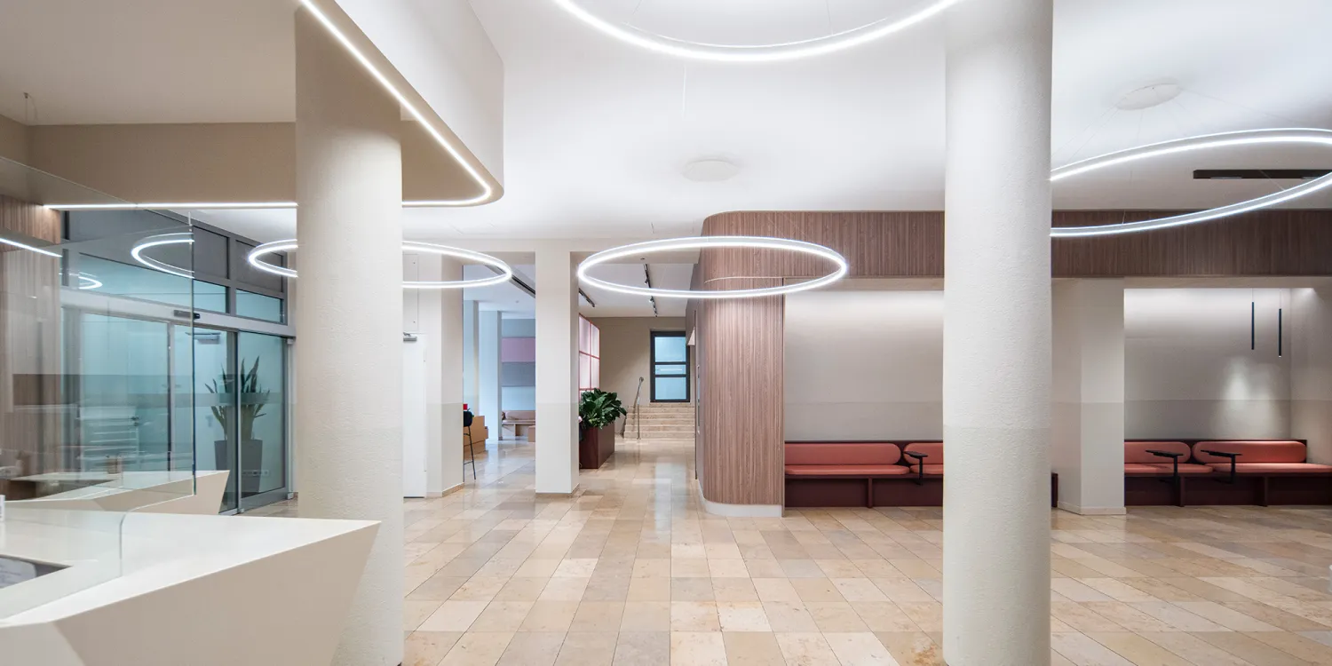 Bürgerhospital – Empfangsbereich mit Holzverkleidung, Kreislicht und geometrischem Tresen.