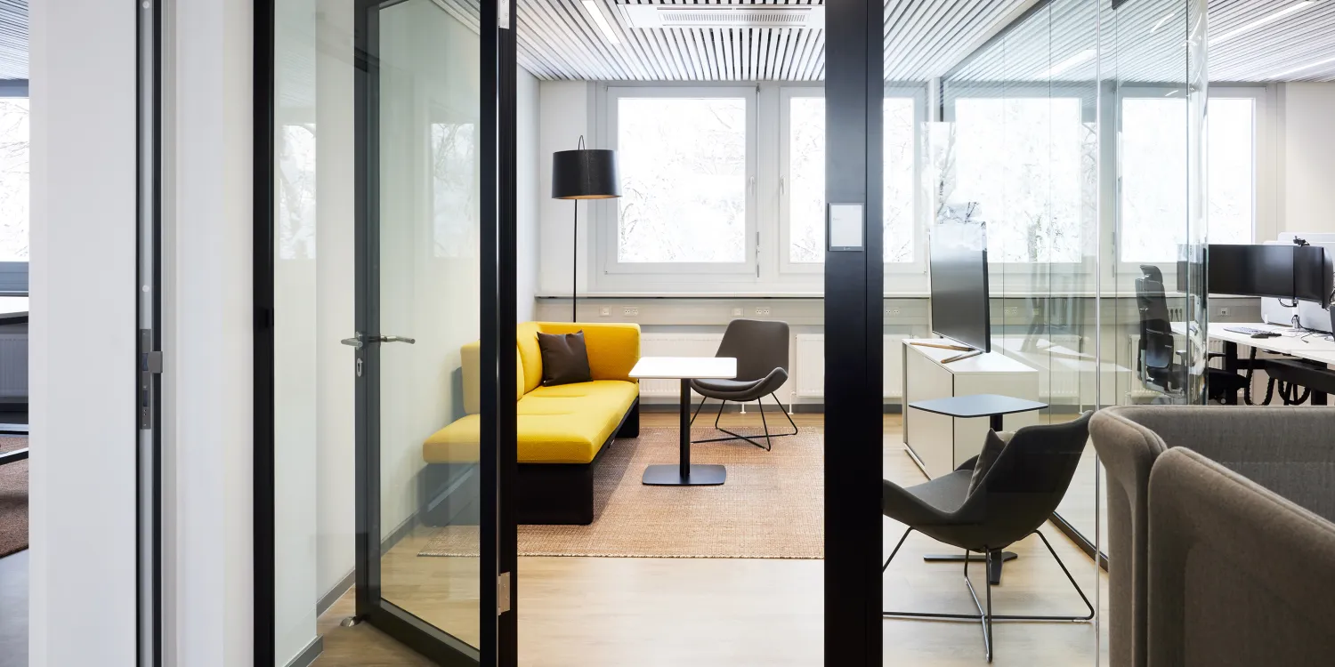 Energieunternehmen: Besprechungsbereich mit gelbem Sofa, schwarzem Sessel und Glastrennwänden.