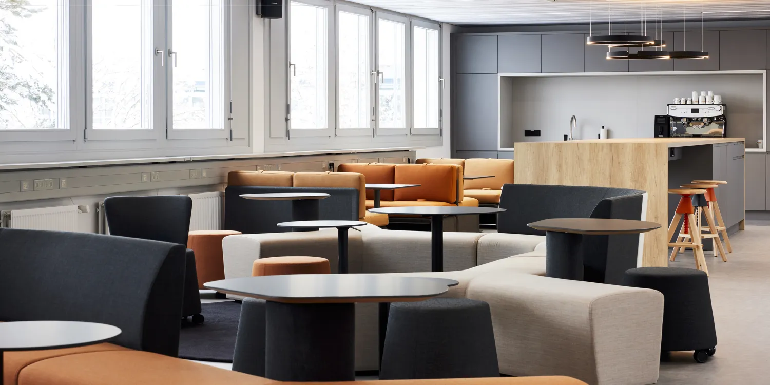 Energieunternehmen – Lounge mit grauen Sesseln, grauen Poufs und Küchenzeile im hinteren Bereich.