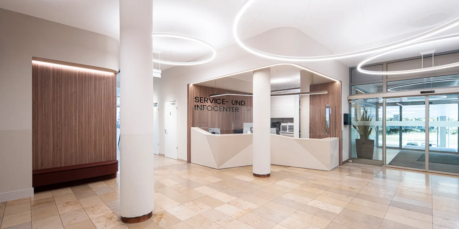 Bürgerhospital – Empfangsbereich mit Holzverkleidung, Kreislicht und geometrischem Tresen.