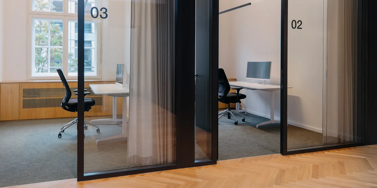 Offene Flur mit Glasbüros. Einzelzimmer mit Schreibtischstuhl und Schreibtisch.