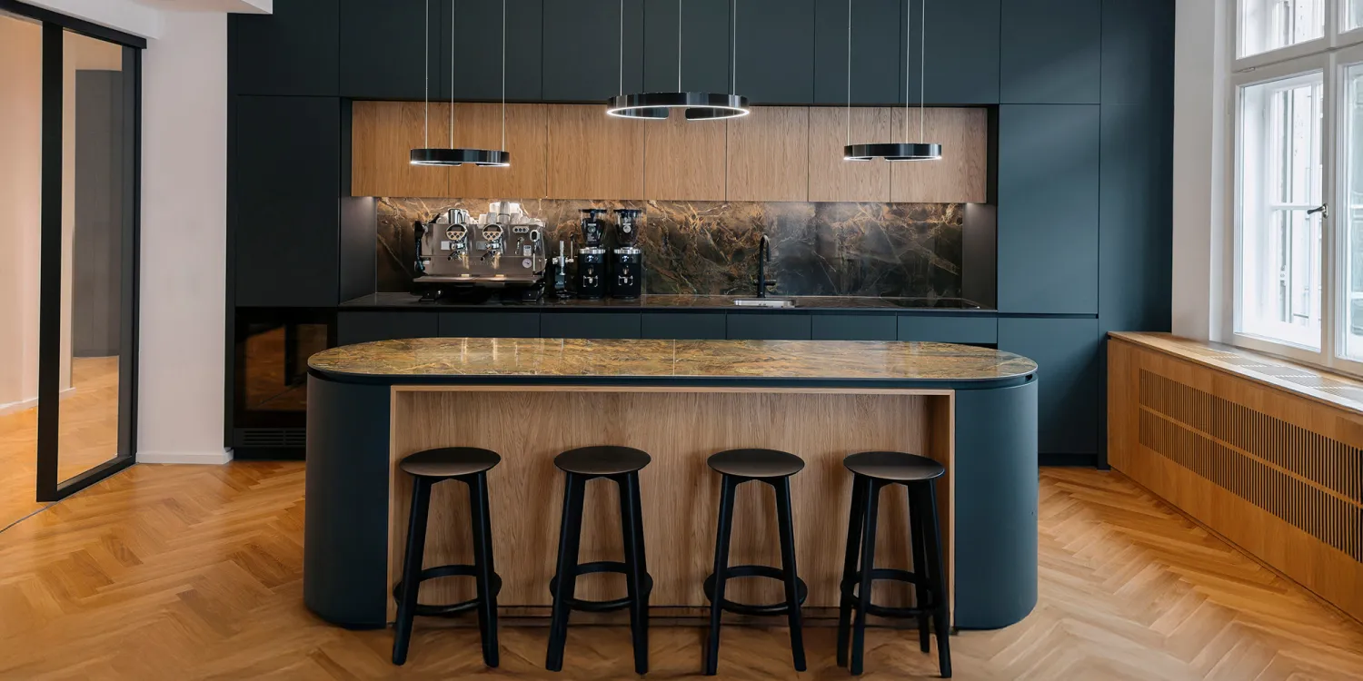 Offene Lounge mit großer Tafel, schwarzer Küche und Glasbüros im Hintergrund