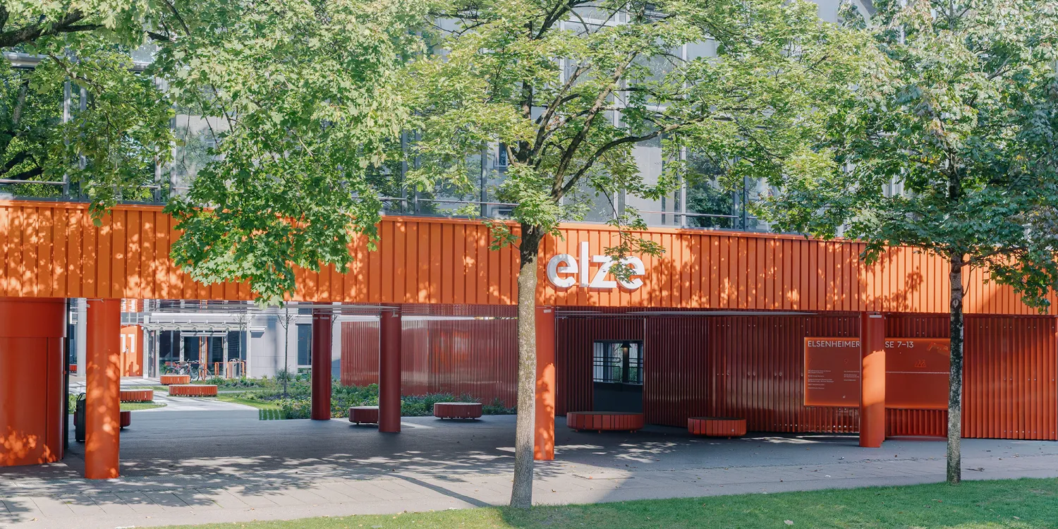 Elsenheimerstraße – überdachter Eingangsbereich mit leuchtend oranger Architektur und runden Sitzbänken.