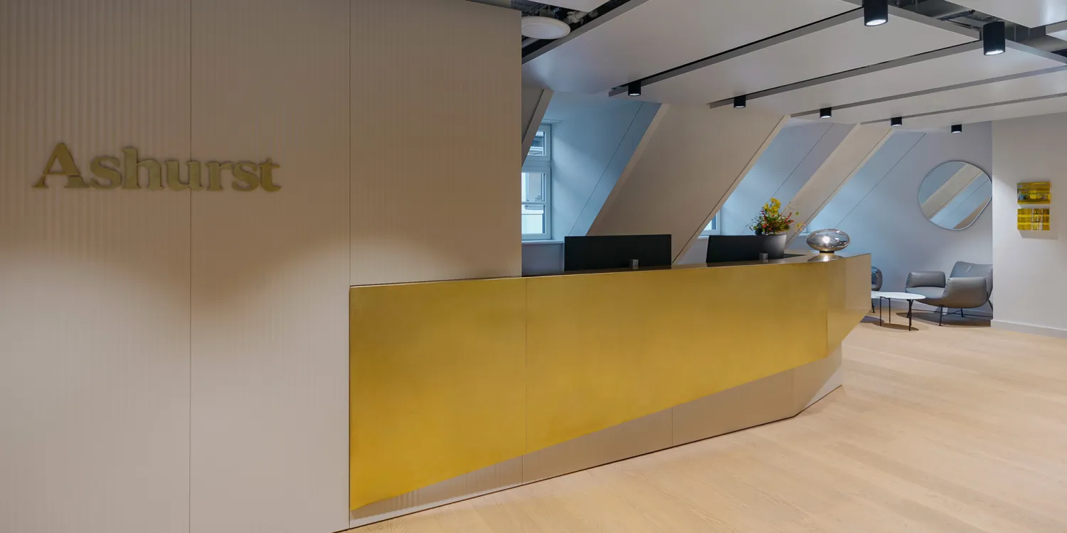 Ashurst München: heller Empfangsbereich mit goldener Theke und loungeartigen Sitznischen.