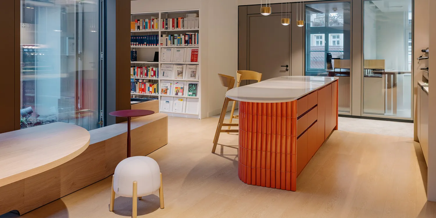 Ashurst München: heller Raum mit oranger moderner Theke  in der Mitte und Bücherregal im Hintergrund