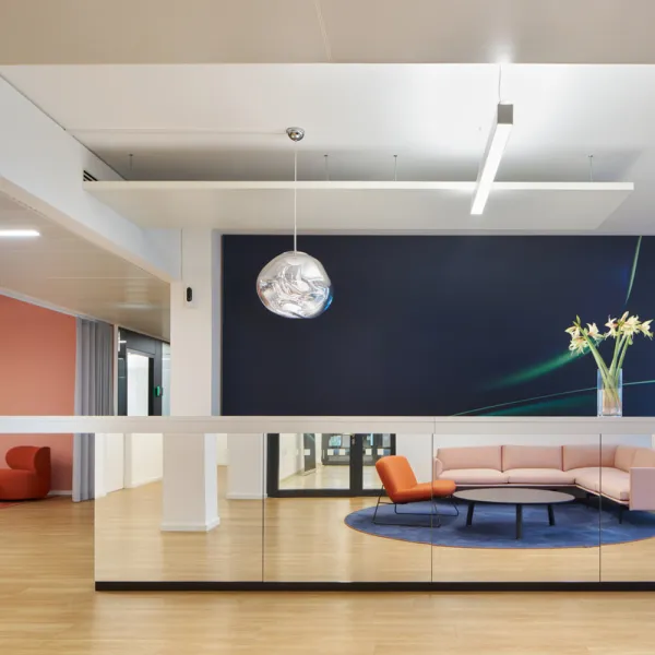 Elegante Lounge mit rosa Sofa, orangefarbenem Sessel, Spiegeltheke, Holzfußboden und skulpturaler Lampe.