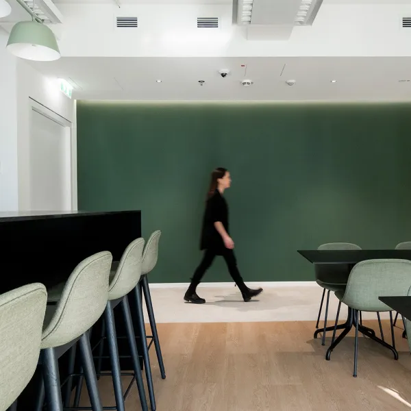 Guidehouse Sonycenter Berlin: Raum mit Sitzmöglichkeiten auf Barhocker oder Stuhl mit einer grünen Wand im Hintergrund