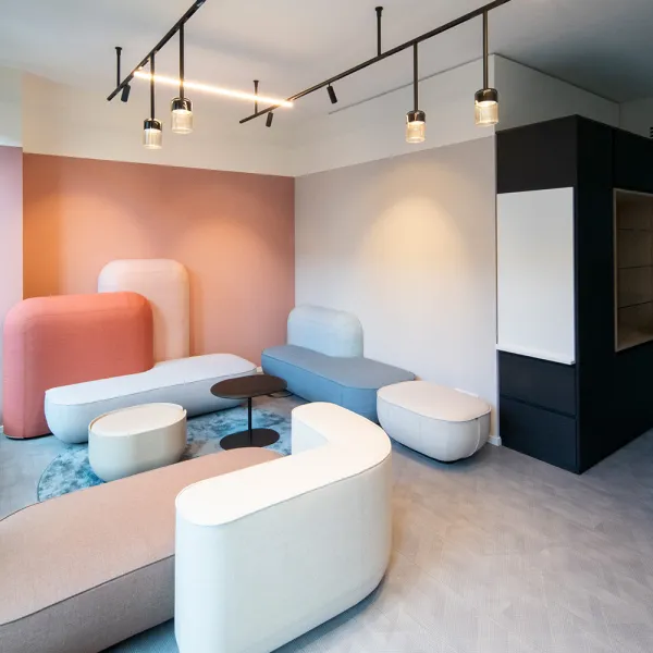 Maxon Follow – Loungebereich mit pastellfarbenen Polstermöbeln und minimalistischer Beleuchtung.