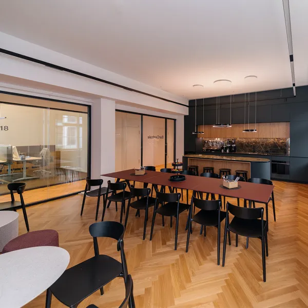 Offene Lounge mit großer Tafel, schwarzer Küche und Glasbüros im Hintergrund