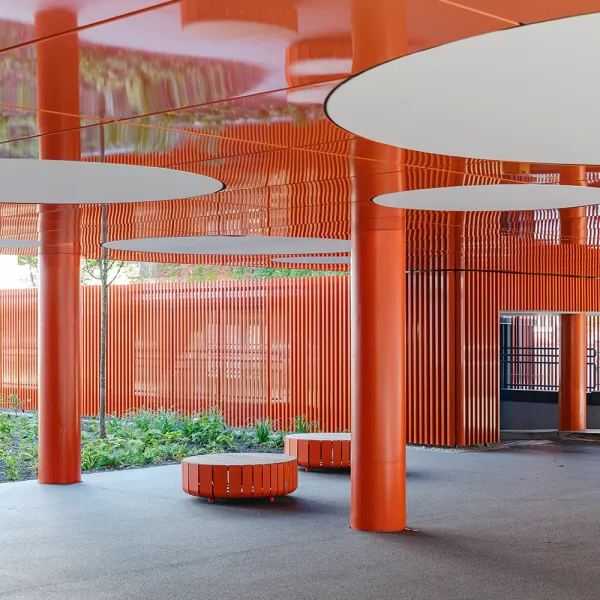 Elsenheimerstraße – überdachter Eingangsbereich mit leuchtend oranger Architektur und runden Sitzbänken.