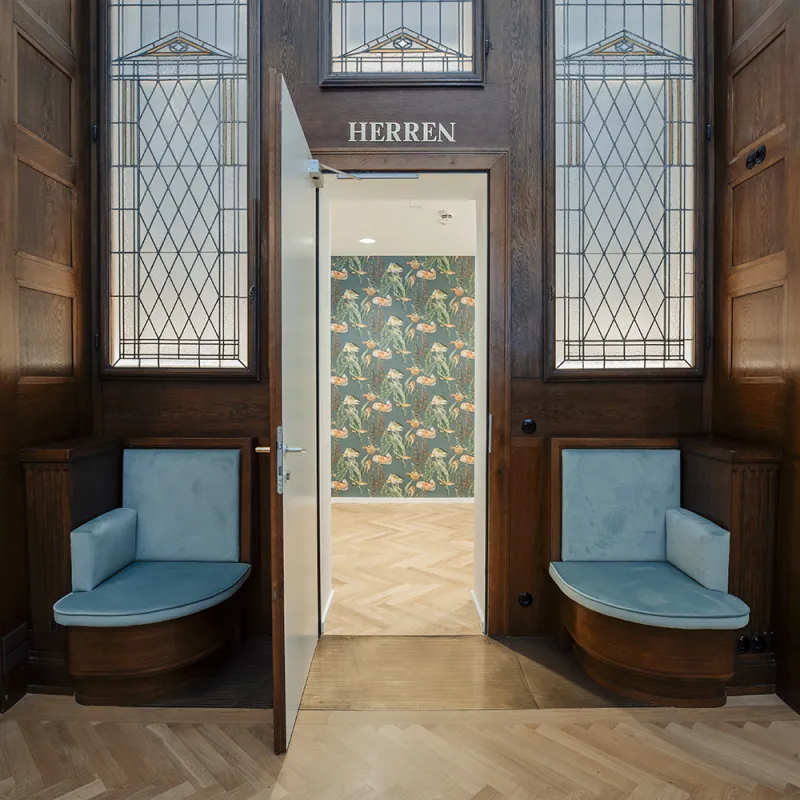 DLA Piper Wien: Historische Sitznische mit blauen Polstern, verglasten Türen und Blick auf modernes Interieur