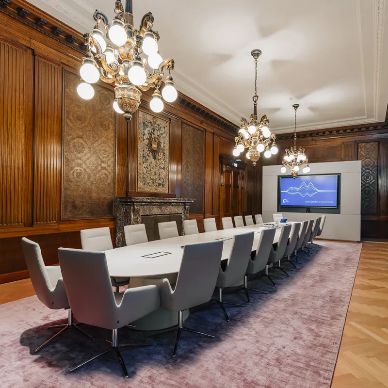 DLA Piper Wien: Edler Konferenzraum mit Holzvertäfelung, großem Tisch, Kronleuchtern und Bildschirm.