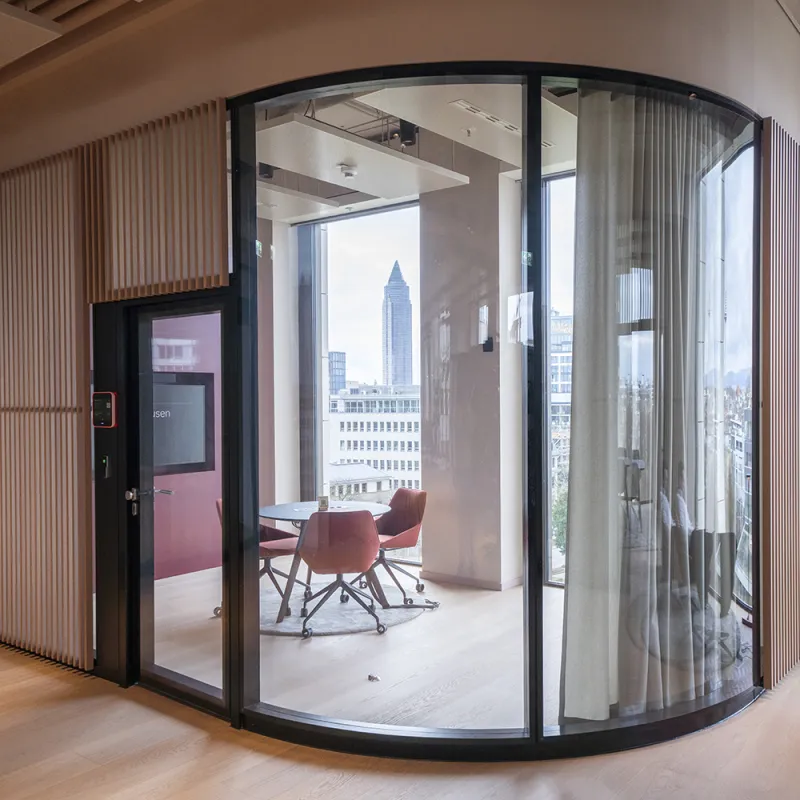Runder Meetingraum mit Glasfront und Vorhängen für flexible Privatsphäre, mit Panoramablick auf Frankfurt.