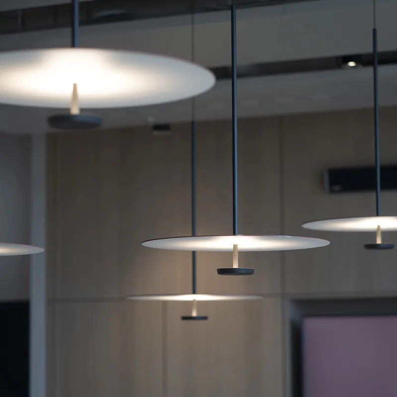Detailaufnahme moderner Pendelleuchten mit diffuser Lichtverteilung, schwebend über einem eleganten Konferenzraum.