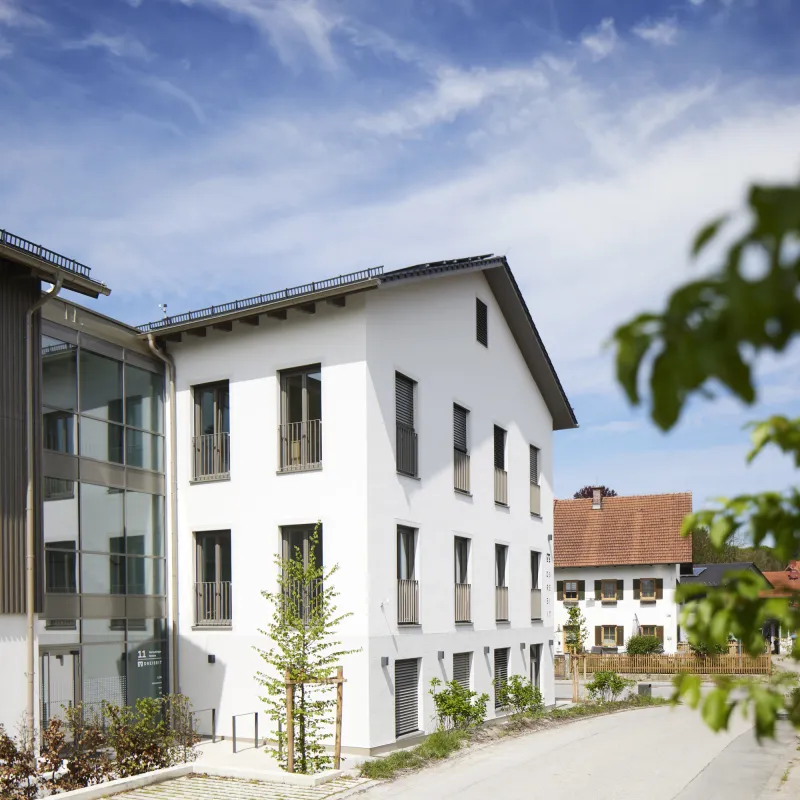 Historischer Gebäudeteil der VR Bank Andechs mit weißer Fassade, modernen Fenstern und Begrünung.