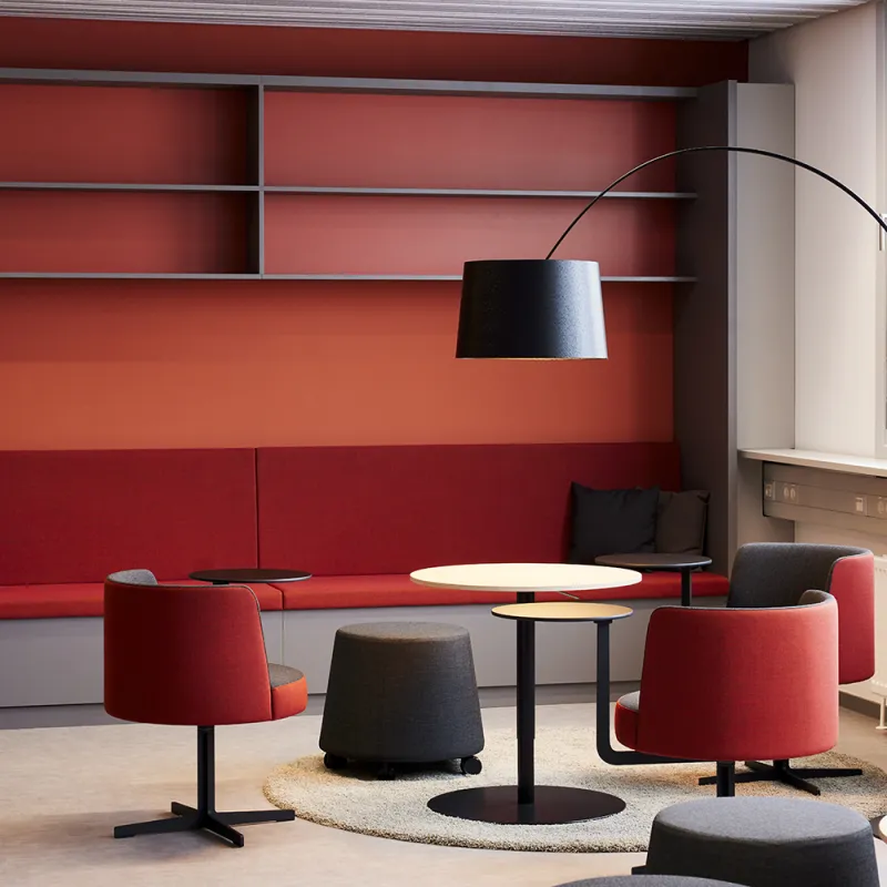 Lounge mit roten Sesseln, grauen Poufs und schwarzer Bogenlampe.