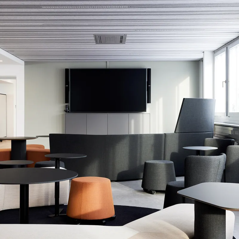 Energieunternehmen – Lounge mit grauen Sesseln, grauen Poufs und Monitor an der Rückwand.