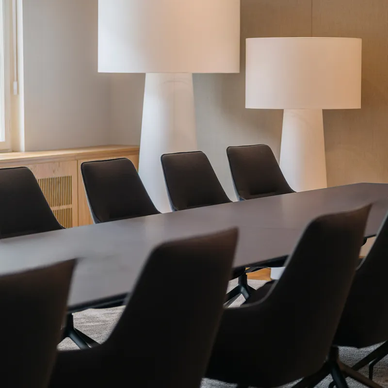Eleganter Konferenzraum mit dunklem Tisch, schwarzen Sesseln und großen weißen Lampen.