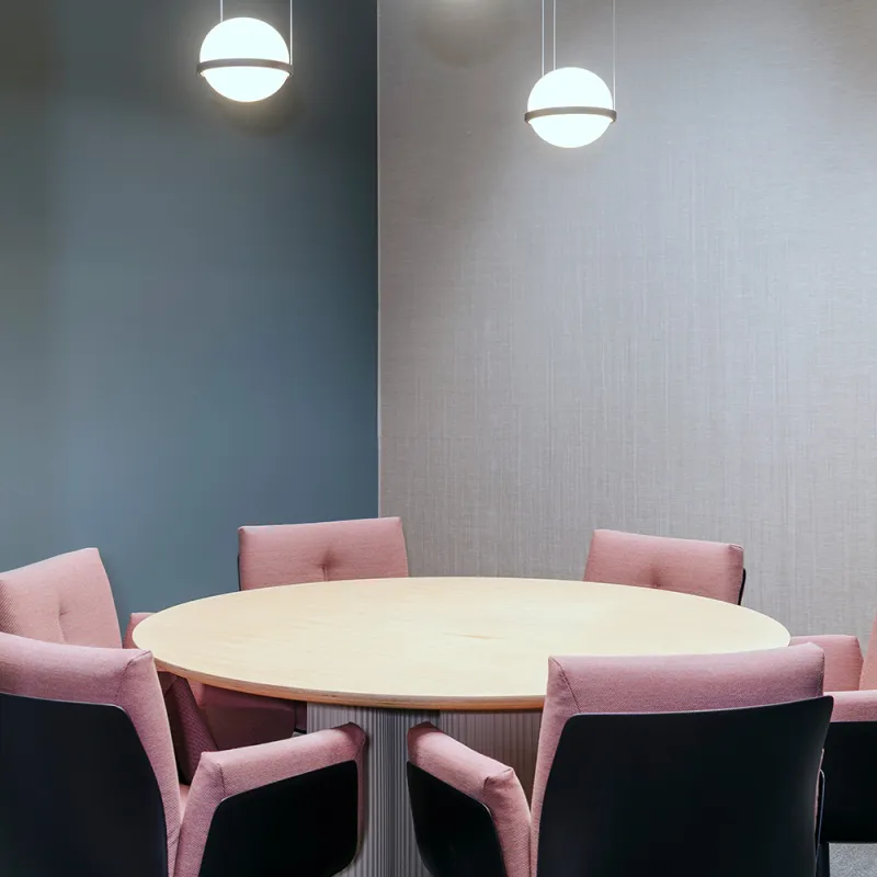Wirtschaftskanzlei – Bürointerieur: Nahaufnahme eines Besprechungszimmer mit rundem Tisch und rosa Sitzmöbeln.