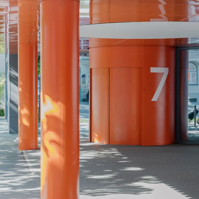 Elsenheimerstraße – überdachter Eingangsbereich mit leuchtend oranger Architektur und Säulen.